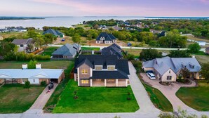 A large, single-story house with a dark roof, surrounded by a well-maintained lawn and a view of a body of water.