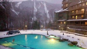 A swimming pool with a view of mountains, surrounded by a building with multiple balconies. - Spruce  Peak resort Ski In/Outwith great views (Stowe)