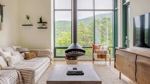 A living room with a large window, a fireplace, a sofa, a coffee table, and a TV. - Spruce  Peak resort Ski In/Outwith great views (Stowe)