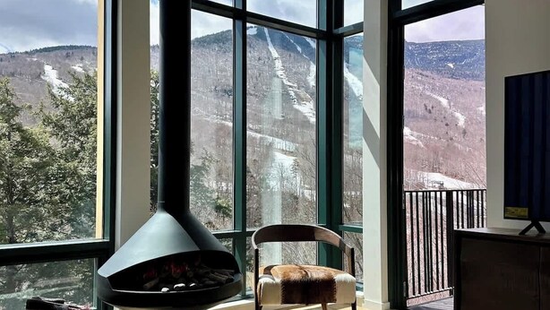 A modern living room with large windows, a fireplace, a sofa, and a coffee table. - Spruce  Peak resort Ski In/Outwith great views (Stowe)