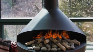 A modern fireplace with a clear view of a snowy landscape through a window. - Spruce  Peak resort Ski In/Outwith great views (Stowe)