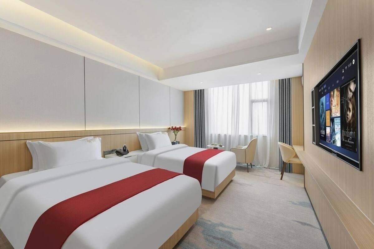 A hotel room with two beds, a TV mounted on the wall, and a desk with a chair.