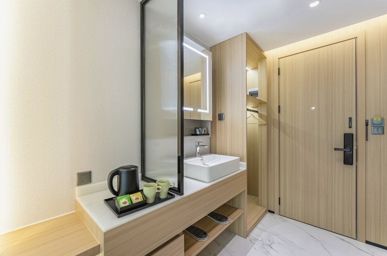Uma casa de banho moderna com um espelho grande, uma pia e uma máquina de café. Há armários de madeira e uma porta com fechadura.