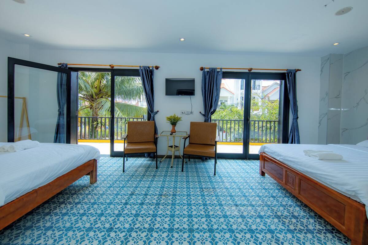 A hotel room with two beds, a balcony with a view, and a small table with chairs.