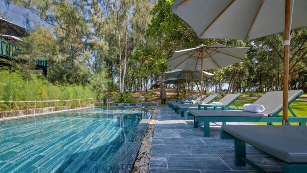 A swimming pool with lounge chairs and umbrellas, surrounded by trees. - Azure Beach Hotel (Da Nang)