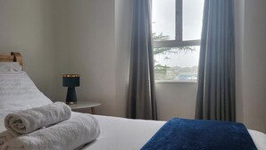 Ein Hotelzimmer mit Bett, Nachttisch, Lampe und Blick nach draußen.