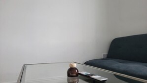 Ein Glastisch mit Fernbedienung und einem dekorativen Gegenstand mit der Aufschrift 'Lounge' in einem Raum mit dunkelgrauem Sofa und einem Bild an der Wand.