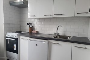 Una cucina con mobili bianchi, un lavello in acciaio inox e un fornello.