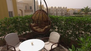 A patio with a round table and two chairs, a hanging chair, and a view of a building with arches and a palm tree.