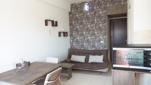 A compact living space with a stone wall, a brown sofa, a dining table with chairs, and a kitchenette with a microwave.