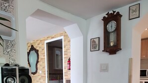 Ein Wohnzimmer mit Holzboden, einer schwarzen Unterhaltungseinheit, einem rosa Teppich und einem Esstisch. Durch einen offenen Durchgang ist eine Küche zu sehen.