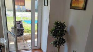 Ein Zimmer mit einer Schiebeglastür, die auf eine Terrasse mit Tisch und Stühlen, einem Blumentopf und einem gerahmten Bild führt.