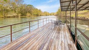 Una terraza de madera con barandas de metal que da a un río, rodeada de árboles.