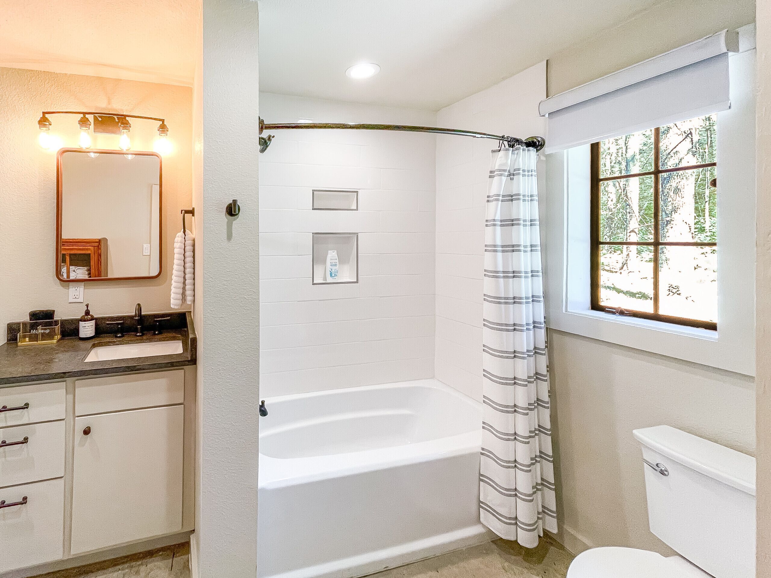 A bathroom with a bathtub, toilet, and a window with a view of trees.