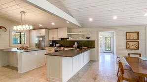 Una cocina moderna con armarios blancos, una isla central y un comedor con sillas de madera.