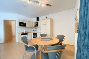 Une cuisine moderne avec des meubles blancs, un four à micro-ondes et une cuisinière. On y trouve une table à manger avec quatre chaises et un rideau bleu sur le côté droit.