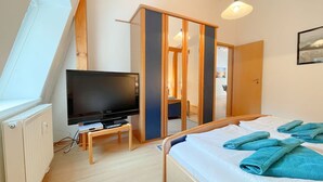 Quarto com televisão em móvel, cama com toalhas azuis e guarda-roupa com porta de correr.