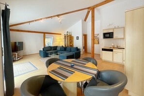 Un espace de vie moderne comprenant un coin repas, un ensemble de canapés, une cuisine et un téléviseur.