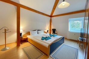 Une chambre à coucher comprenant un lit, deux tables de chevet, une chaise, une lampe sur pied, une fenêtre et un radiateur.