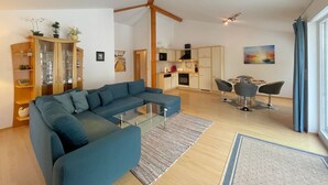 Uma sala de estar moderna com um sofá seccional, uma mesa de centro de vidro e um espaço de jantar com duas cadeiras.