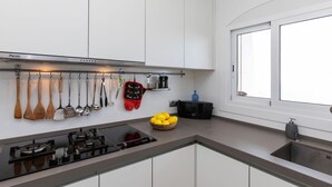 A modern kitchen with white cabinets, a gas stove, and various utensils hanging on the wall. - Apartment Pardal by Interhome (Llançà)