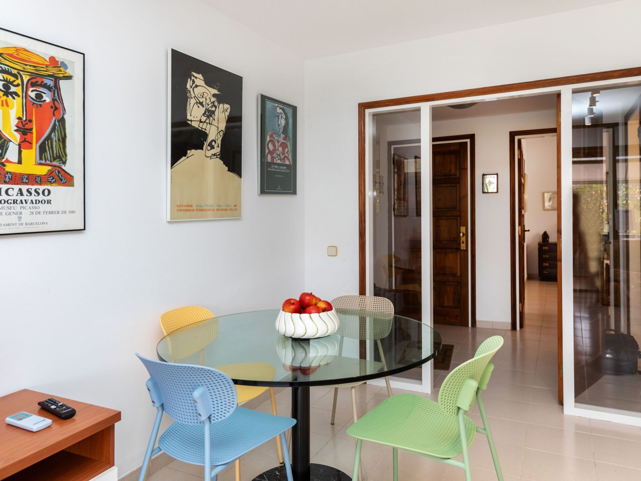 A dining area with a glass table, colorful chairs, and artwork on the wall.