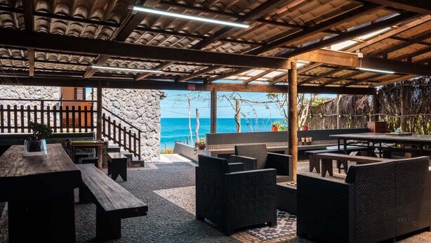 An outdoor seating area with wooden tables and wicker furniture, overlooking a scenic view of the ocean. - GuestReady - Magical refuge in Madeira (Seixal)