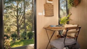 Una habitación con vistas a un bosque, una mesita con una planta, una silla y un interruptor de luz en la pared.