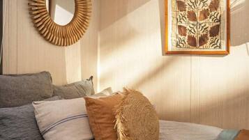 A bedroom with a bed, pillows, a woven throw, a mirror, and a wall-mounted air conditioner.