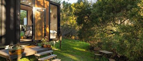 Una cabaña moderna y compacta con terraza de madera, mobiliario exterior y jardín.