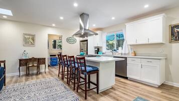 A modern kitchen with white cabinetry, a central island, bar stools, and a patterned rug.