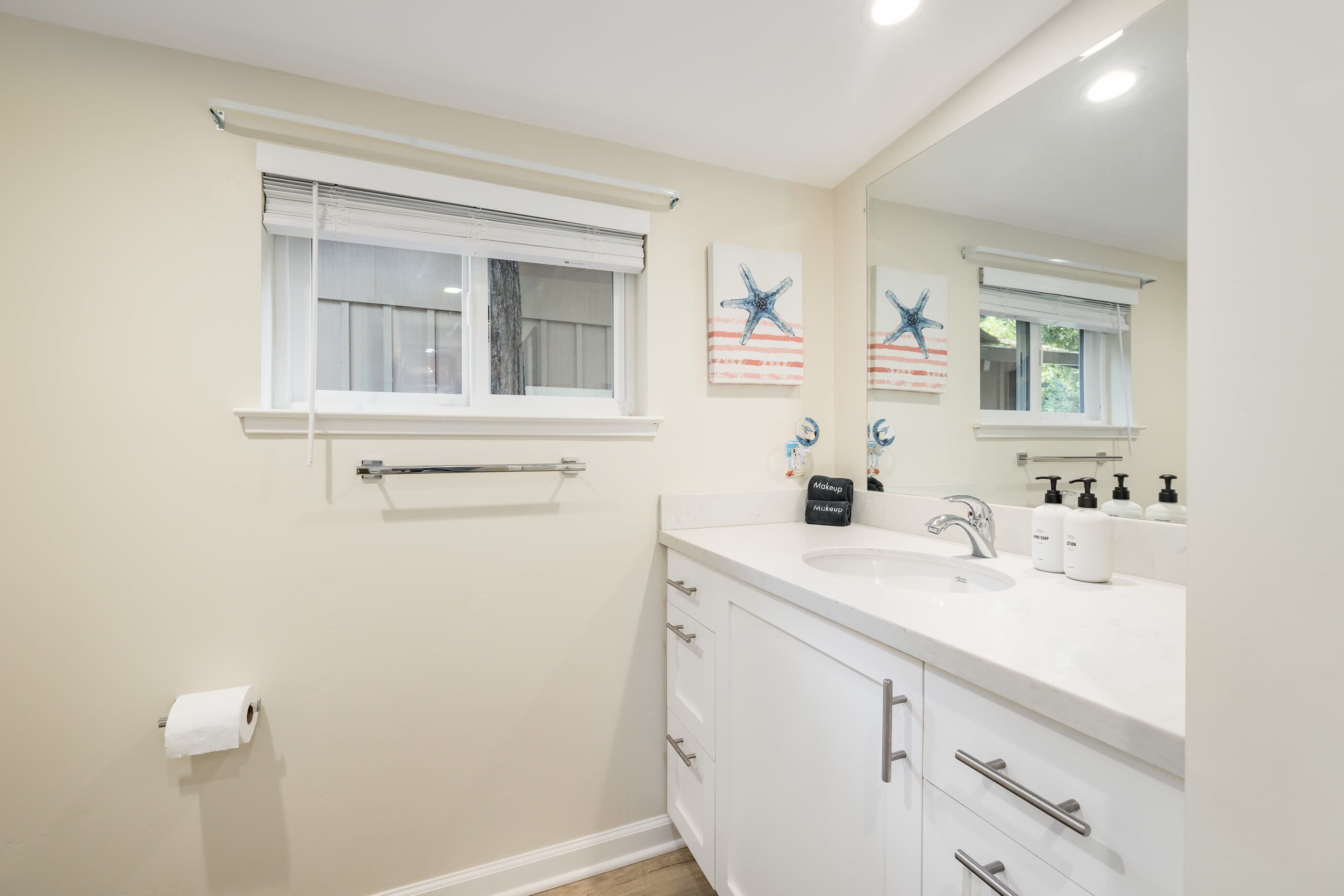 A bathroom with a white sink, vanity, and a large mirror.