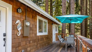 A wooden deck with a door, a mailbox, a power box, and a table with chairs. - Redwood Home - view of the river! (Ben Lomond)