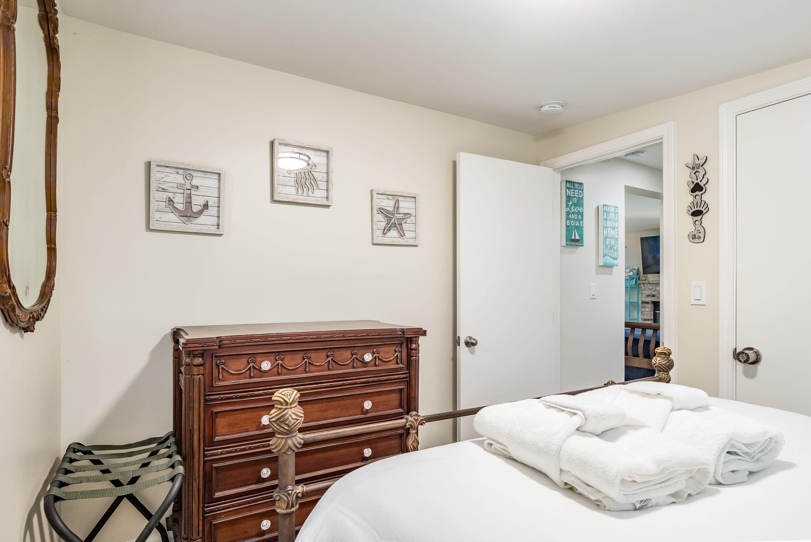 Un dormitorio con un aparador de madera, una cama con ropa de cama blanca y tres cuadros náuticos colgados en la pared.