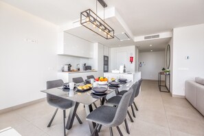 A modern dining area with a glass table, grey chairs, and a pendant light.