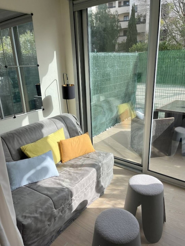 A modern living room with a grey sofa, two cushions, a small table, and two grey stools.