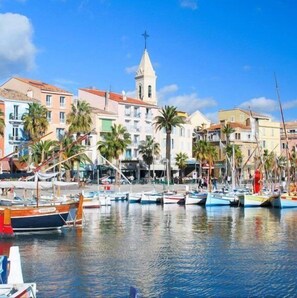 A marina with boats docked, a prominent church tower, and colorful buildings along the waterfront.