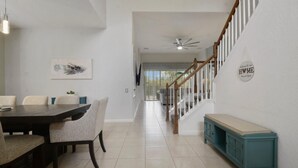 A spacious dining area with a dark wooden table and light-colored chairs, leading to a staircase with a white railing and a ceiling fan.