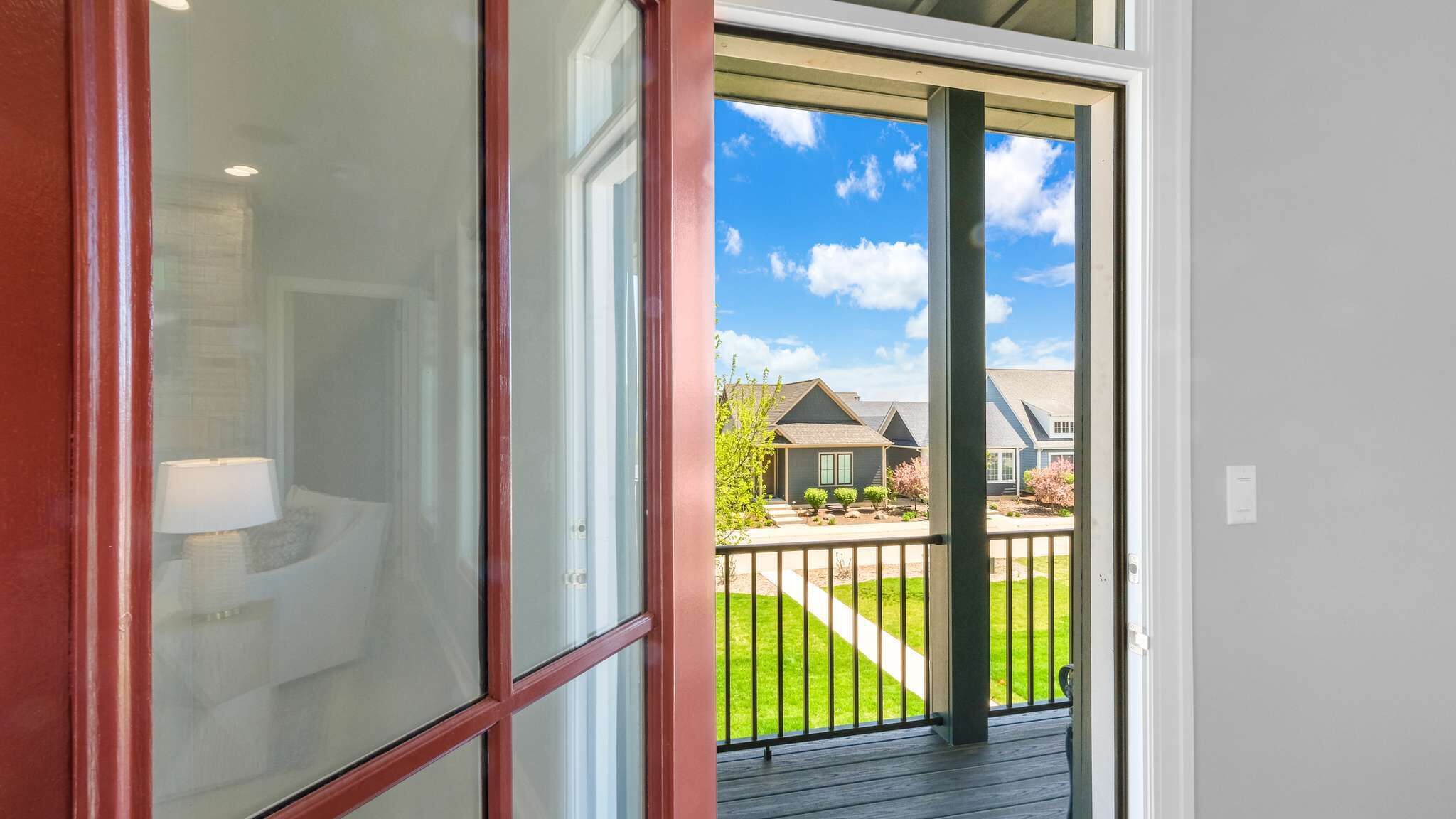 Une vue à travers une porte vitrée donnant sur un quartier résidentiel, avec une pelouse, une clôture et des maisons en arrière-plan.