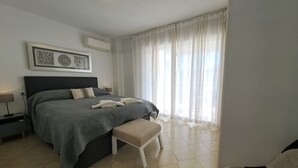 A bedroom with a bed, bedside tables, a bench, a wall-mounted air conditioner, and a window with sheer curtains. - Ref: 324 Centric 3 bedroom apartment with swimming pool and close to everything (Fuengirola)