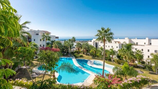 Un resort con una amplia piscina rodeada de palmeras y vistas al océano.