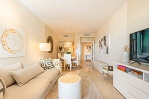 A modern living room with a sofa, a round coffee table, and a TV stand. - Hoyo 3 | Marbella Resort Golf Pools Apartment (Benahavís)