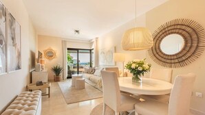 Una sala moderna con una mesa redonda para comer, sillas blancas, un sofá y un amplio ventanal con vistas al exterior.