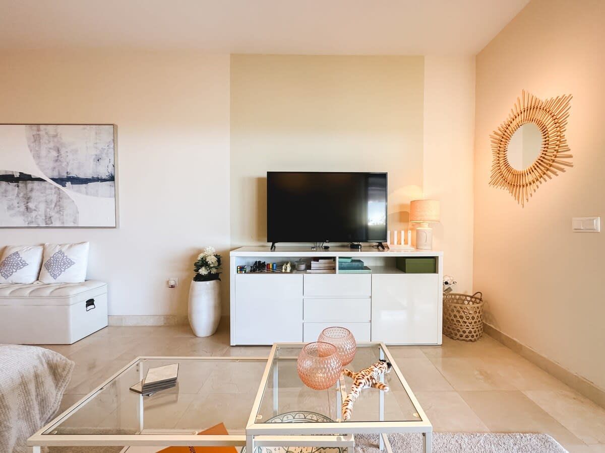 A modern living room with a flat-screen TV, white furniture, and decorative items.