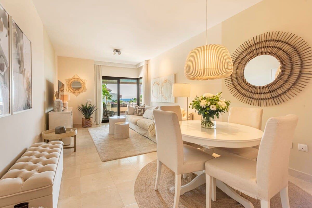 A modern living room with a round dining table, white furniture, and a view to the outside.