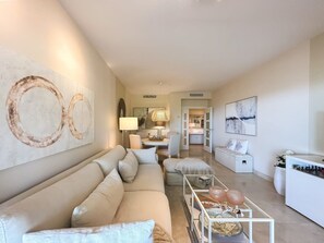 A modern living room with a sofa, coffee table, and artwork on the walls. - Hoyo 3 | Marbella Resort Golf Pools Apartment (Benahavís)