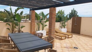 An outdoor patio with a table and chairs, a wooden bench, and potted plants. - Las Brisas | Penthouse Rooftop Terrace Pool Family Only (Marbella)