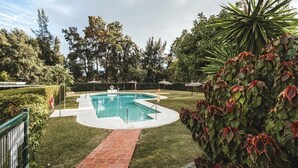 Una piscina amb un camí de maó que hi mena, envoltada d'herba ben cuidada i arbres.