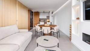 Un saló modern amb un sofà, una taula rodona de menjador amb cadires, una llar de foc i una cuina al fons.