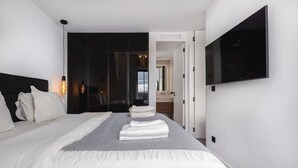 Habitació d'hotel moderna amb un llit gran, un televisió de pantalla plana penjada a la paret i vista a la ciutat per la finestra.